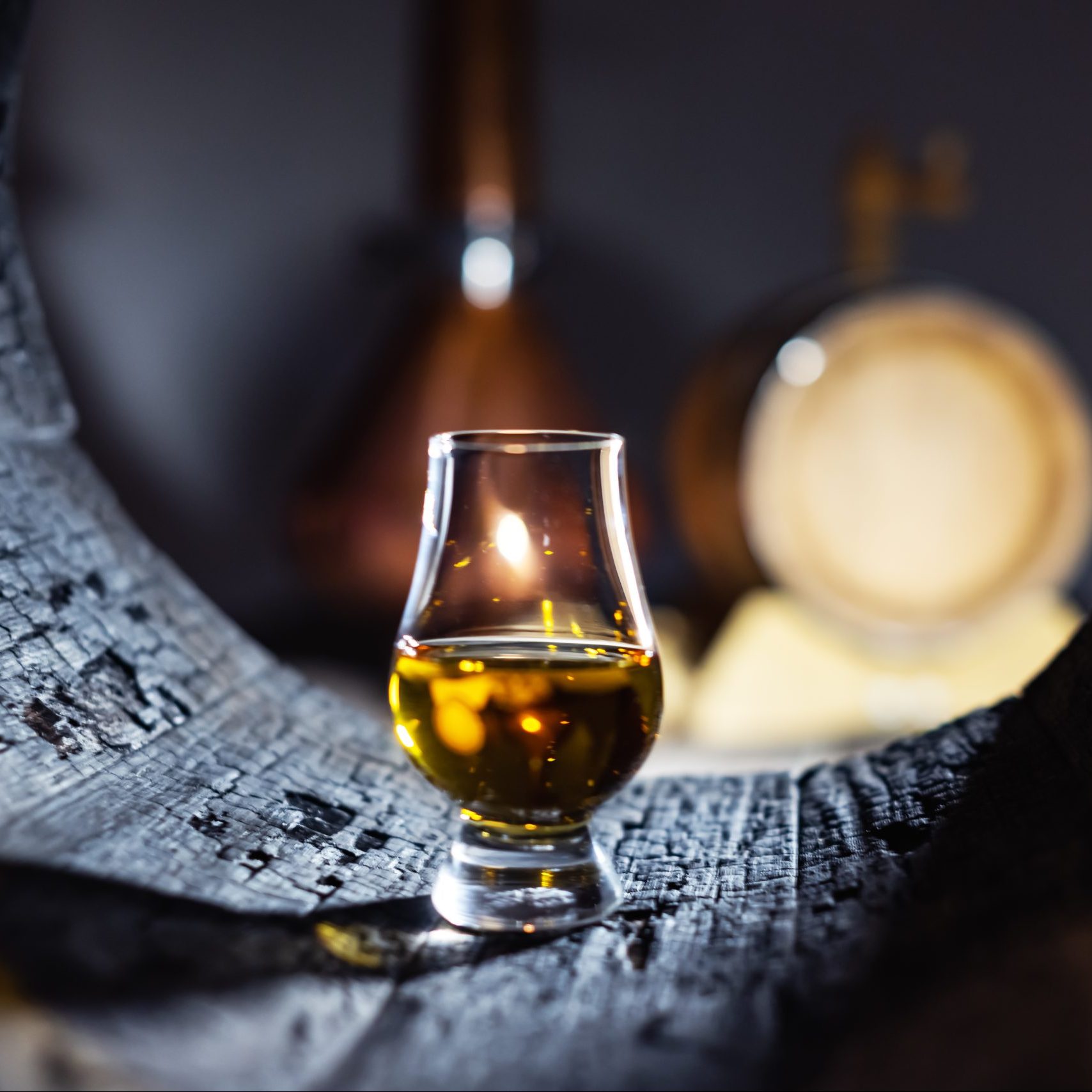 A glass of whiskey in old oak barrel. Copper alambic on background. Traditional alcohol distillery concept